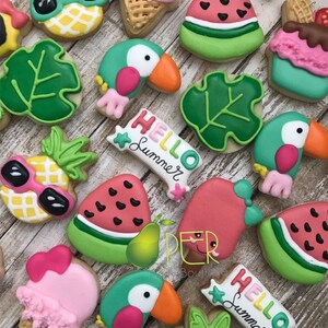 May include: A collection of decorated sugar cookies in a summer theme. Cookies include a pineapple with sunglasses, watermelon slices, toucans, ice cream cones, and cookies with the text "Hello Summer".