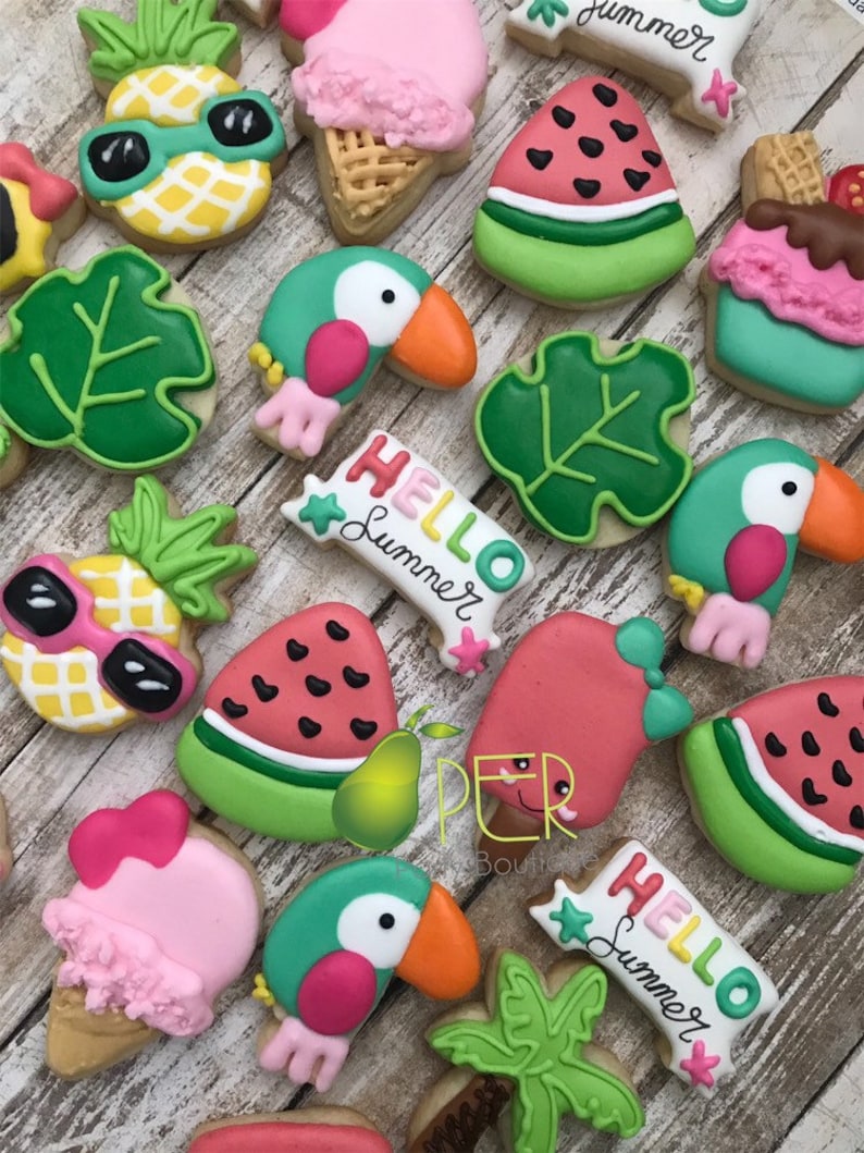 May include: A collection of decorated sugar cookies in a summer theme. Cookies include a pineapple with sunglasses, watermelon slices, toucans, ice cream cones, and cookies with the text "Hello Summer".