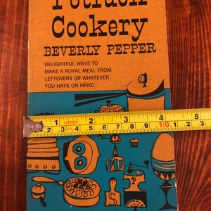 May include: A vintage orange and blue cookbook titled "Potluck Cookery" by Beverly Pepper. The cover features a colourful illustration of kitchen utensils and food.