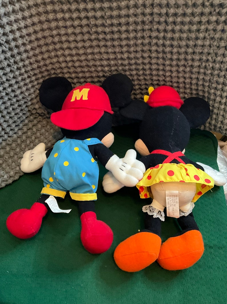 Peut inclure: Une paire de peluches Mickey Mouse et Minnie Mouse. Mickey porte une casquette rouge avec un "M" jaune et une salopette bleue &agrave; pois jaunes. Minnie porte un n&oelig;ud rouge et une jupe &agrave; pois jaunes et rouges.