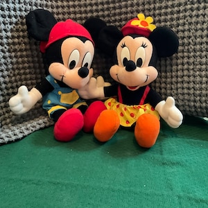 Peut inclure: Une paire de peluches Mickey Mouse et Minnie Mouse. Mickey porte un chapeau rouge, une salopette bleue et une chemise jaune. Minnie porte un chapeau rouge avec une fleur jaune, une robe rouge &agrave; pois jaunes et une chemise jaune.