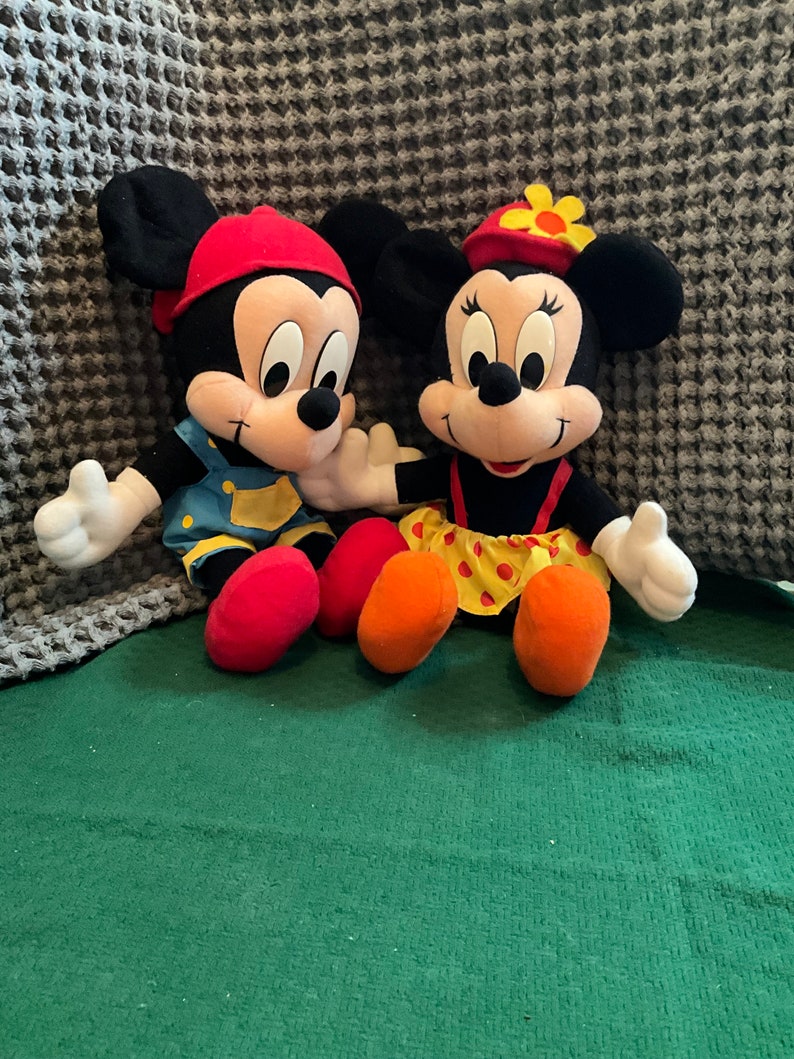 Peut inclure: Une paire de peluches Mickey Mouse et Minnie Mouse. Mickey porte un chapeau rouge, une salopette bleue et une chemise jaune. Minnie porte un chapeau rouge avec une fleur jaune, une robe rouge &agrave; pois jaunes et une chemise jaune.