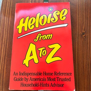 May include: A red book titled "Heloise from A to Z" with yellow lettering and a small flower graphic. The book is a home reference guide by America's Most Trusted Household-Hints Advisor.
