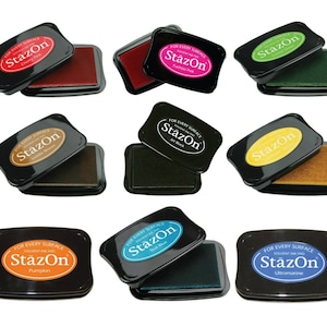 May include: A selection of StazOn solvent ink pads in colours such as Cherry Pink, Jet Black, and Ultramarine. Each pad is in a black case with the brand name and colour label. These pads are designed for use on a variety of surfaces.