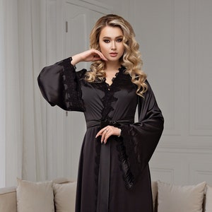 Peut inclure: Une longue robe de satin noire avec des bordures en dentelle et une ceinture assortie. La robe a des manches longues avec de larges poignets et un col en V.