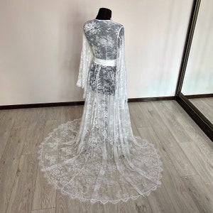 May include: A white lace robe with long, flared sleeves and a floor-length train. The robe is displayed on a mannequin, showcasing the intricate floral lace pattern and a white satin belt. The delicate fabric creates a romantic and elegant aesthetic.