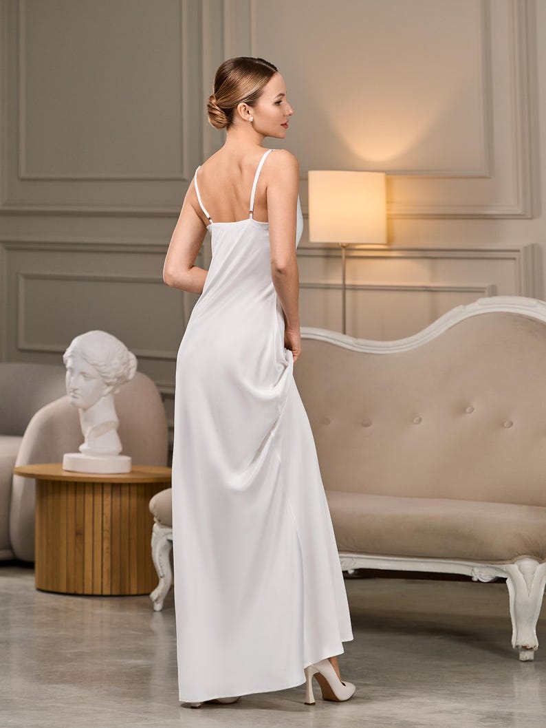 Back view of an ivory slip dress with thin spaghetti straps and a smooth satin finish. The floor-length design elegantly flows to the ground.
