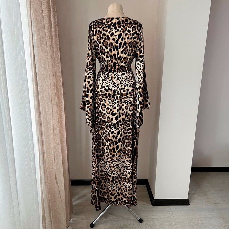 May include: A long, brown and black leopard print maxi dress with a V-neckline and long sleeves. The dress has a tie belt at the waist and a flowing skirt.