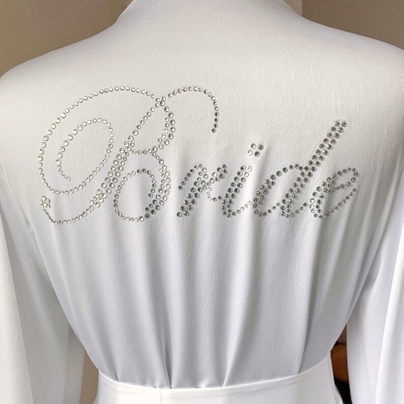Puede incluir: Batista blanca con la palabra "Bride" escrita en pedrer&iacute;a.