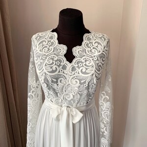 May include: A white lace robe with long sleeves and a satin sash. The robe has a V-neckline and a delicate floral pattern.