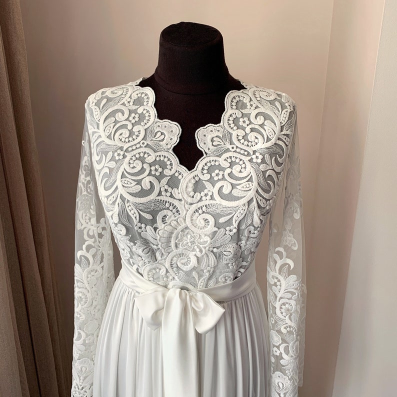 May include: A white lace robe with long sleeves and a satin sash. The robe has a V-neckline and a delicate floral pattern.