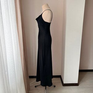 K&ouml;nnte beinhalten: Ein schwarzes, &auml;rmelloses Maxikleid mit einem Cowl-Ausschnitt und einer figurbetonten Silhouette.
