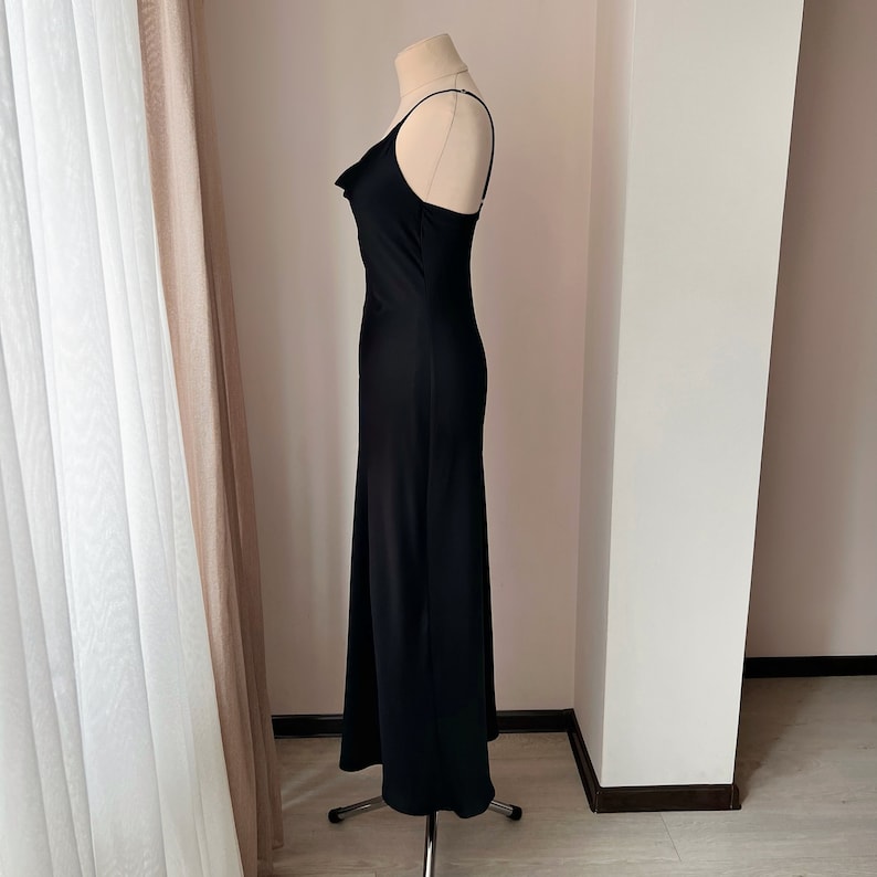 K&ouml;nnte beinhalten: Ein schwarzes, &auml;rmelloses Maxikleid mit einem Cowl-Ausschnitt und einer figurbetonten Silhouette.