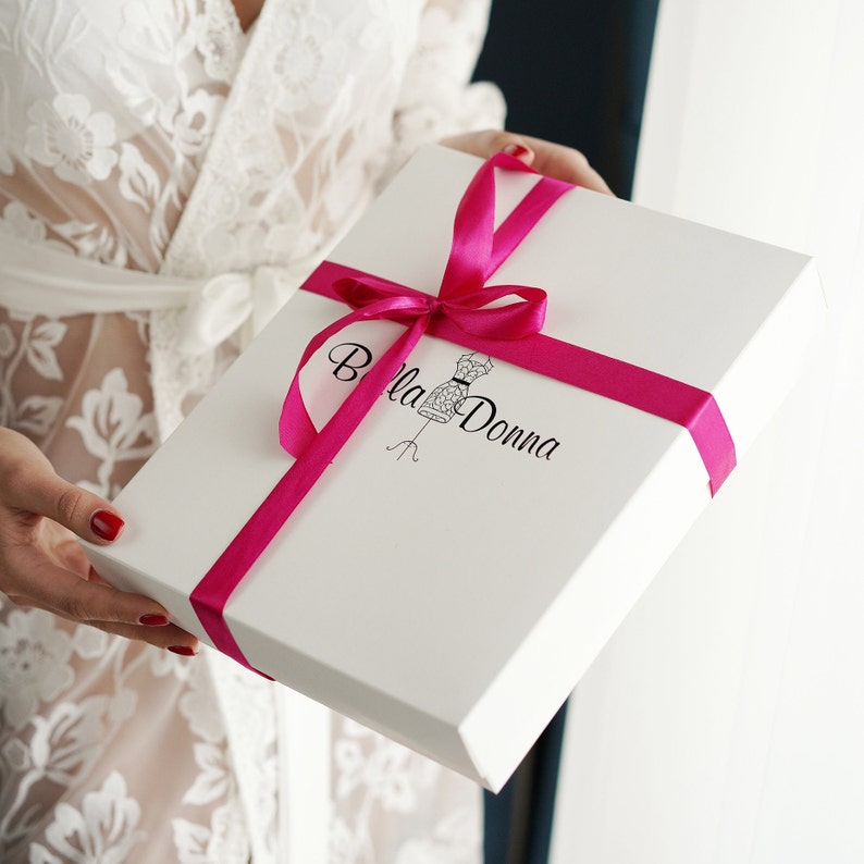 May include: A white gift box with a pink ribbon and bow. The box has a logo that says "Bella Donna" with a stylized image of a dress form.