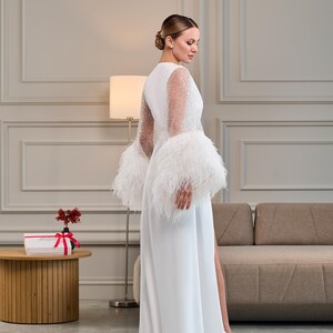 A back view of a long white satin robe with sheer pearl-embellished sleeves and voluminous feather cuffs. The smooth satin drapes gracefully, while the intricate sleeve details add a touch of vintage glamour.