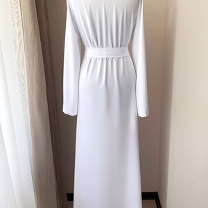 Puede incluir: Un vestido maxi blanco con mangas largas y un cintur&oacute;n de lazo en la cintura.