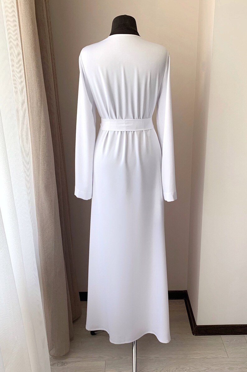 Puede incluir: Un vestido maxi blanco con mangas largas y un cintur&oacute;n de lazo en la cintura.