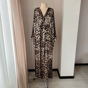 May include: A long, brown and white leopard print maxi dress with a wrap style bodice and long sleeves. The dress has a tie belt at the waist.