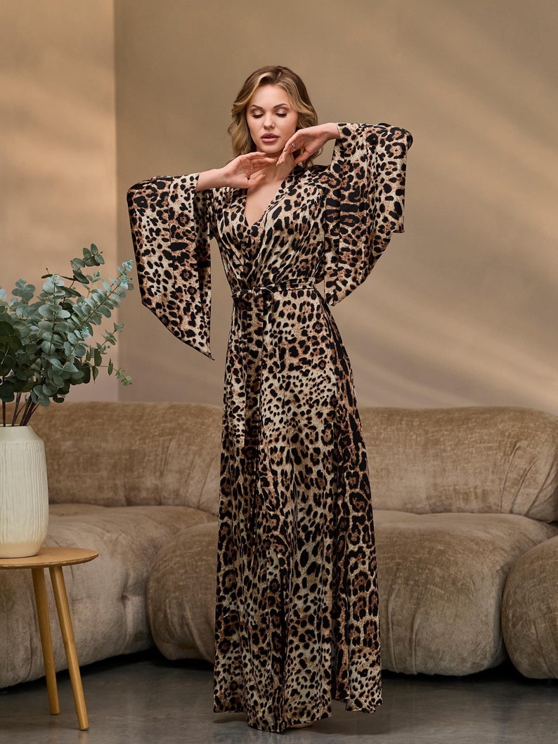 Puede incluir: Un vestido largo y fluido de estampado de leopardo con escote en V y cintur&oacute;n de lazo. El vestido tiene mangas anchas acampanadas y una longitud maxi.