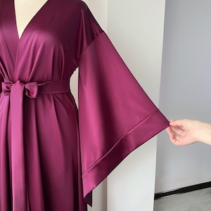 May include: A long, deep purple satin robe with a V-neckline and wide, flowing sleeves. The robe has a sash tie at the waist.
