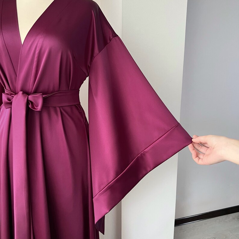 May include: A long, deep purple satin robe with a V-neckline and wide, flowing sleeves. The robe has a sash tie at the waist.