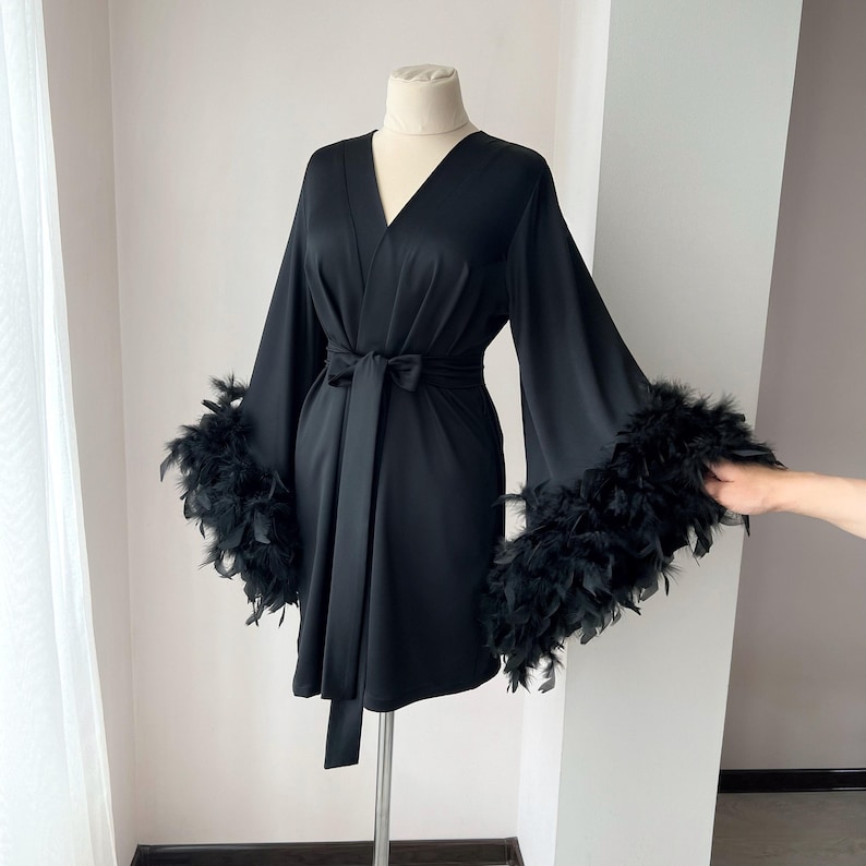 May include: A black satin robe with long sleeves and a wrap closure. The sleeves have black feather trim.