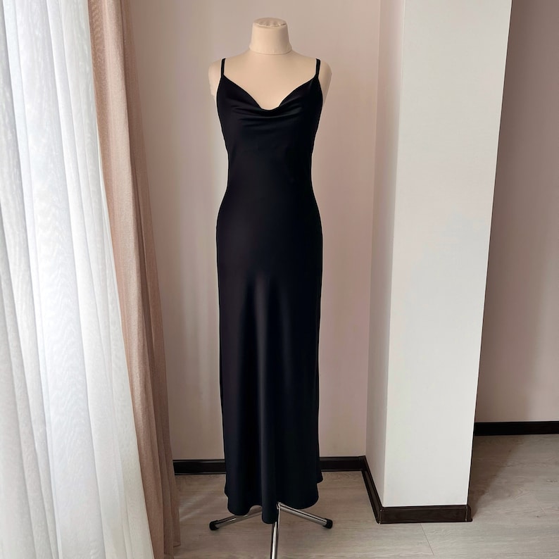 K&ouml;nnte beinhalten: Ein schwarzes, langes, &auml;rmelloses Satin-Kleid mit einem Cowl-Ausschnitt.