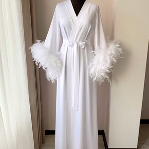 May include: A white robe with long sleeves and a sash. The sleeves have white feather trim.