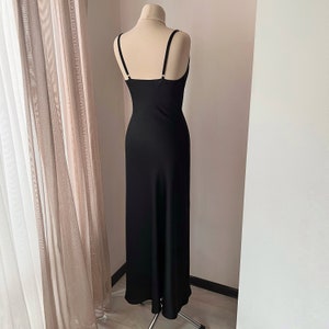 K&ouml;nnte beinhalten: Ein schwarzes Maxikleid mit d&uuml;nnen Tr&auml;gern und einem figurbetonten Oberteil. Das Kleid hat einen flie&szlig;enden Rock und ein schlichtes Design.