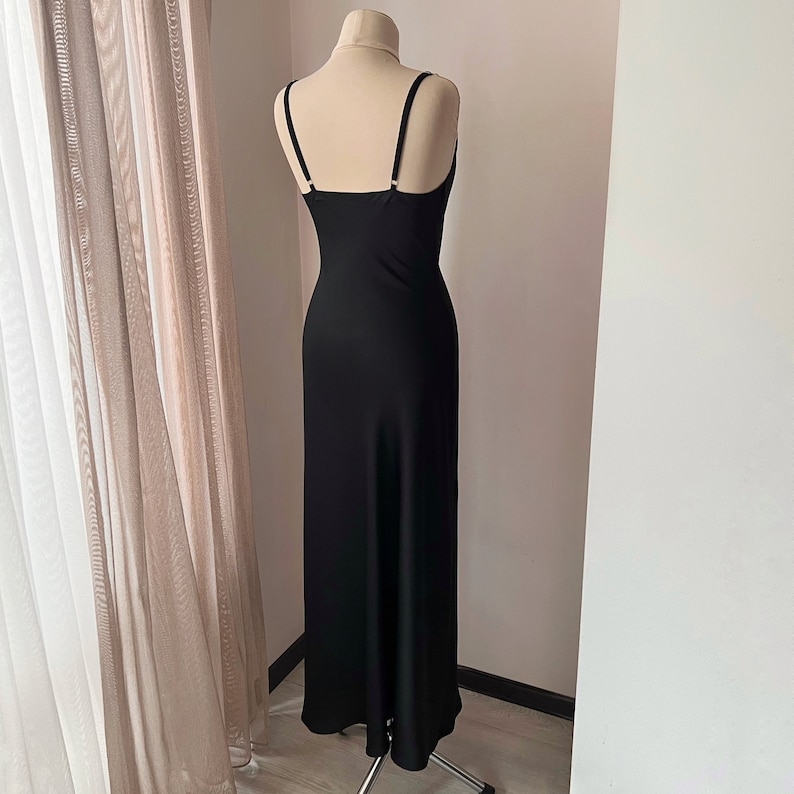 K&ouml;nnte beinhalten: Ein schwarzes Maxikleid mit d&uuml;nnen Tr&auml;gern und einem figurbetonten Oberteil. Das Kleid hat einen flie&szlig;enden Rock und ein schlichtes Design.