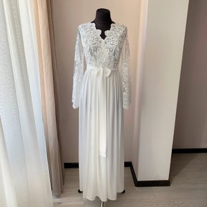 May include: A white lace robe with long sleeves and a V-neckline. The robe has a sash tie at the waist and a flowing skirt.