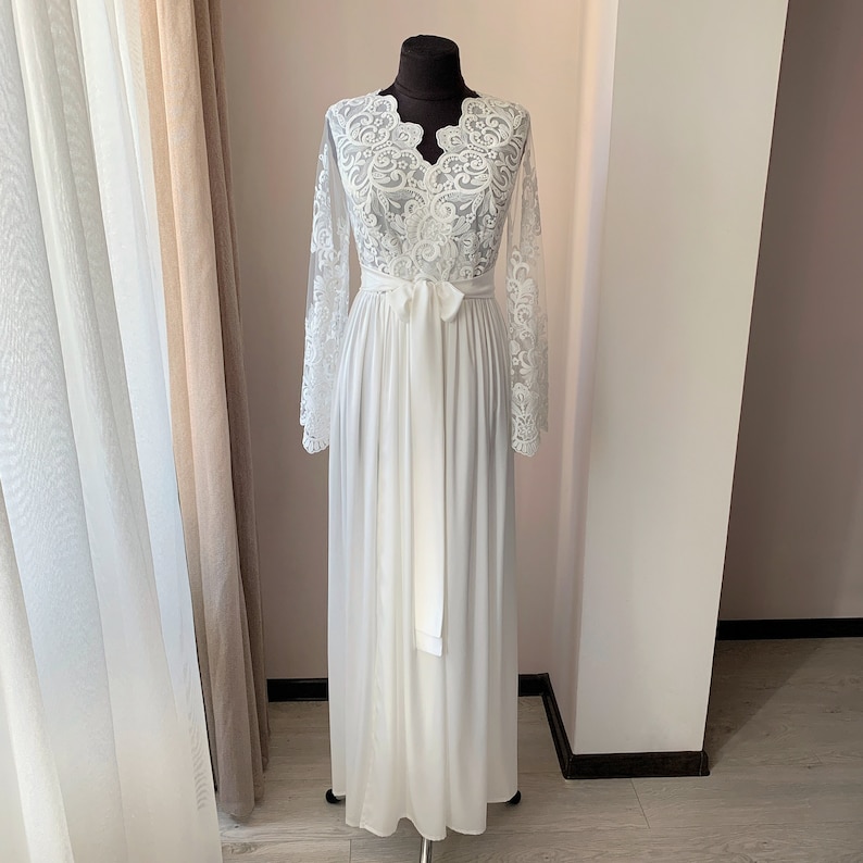 May include: A white lace robe with long sleeves and a V-neckline. The robe has a sash tie at the waist and a flowing skirt.