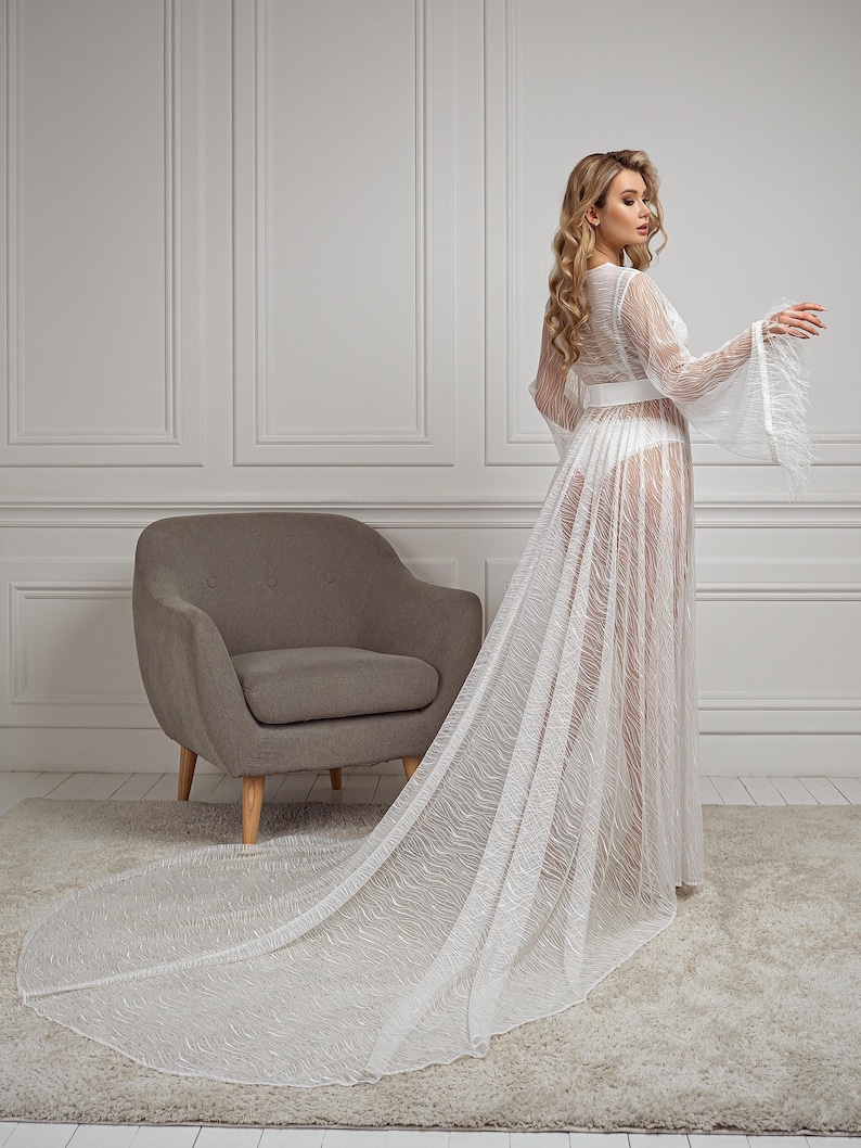 May include: A white sheer robe with a long train and a belt. The robe features a delicate lace pattern and is made from a lightweight fabric.