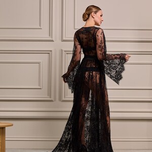 Side view of a model wearing a sheer black lace robe with embroidered floral details and a long flowing train, ideal for special occasions.