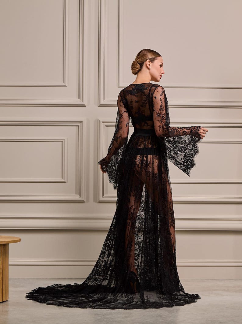 Side view of a model wearing a sheer black lace robe with embroidered floral details and a long flowing train, ideal for special occasions.