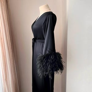 May include: A black satin robe with long sleeves and a sash. The sleeves have black feather trim.