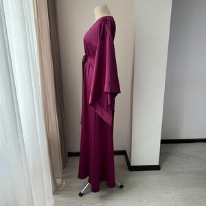 May include: A long, burgundy maxi dress with a V-neckline and wide, flowing sleeves. The dress has a sash tie at the waist.