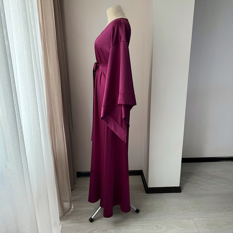 May include: A long, burgundy maxi dress with a V-neckline and wide, flowing sleeves. The dress has a sash tie at the waist.