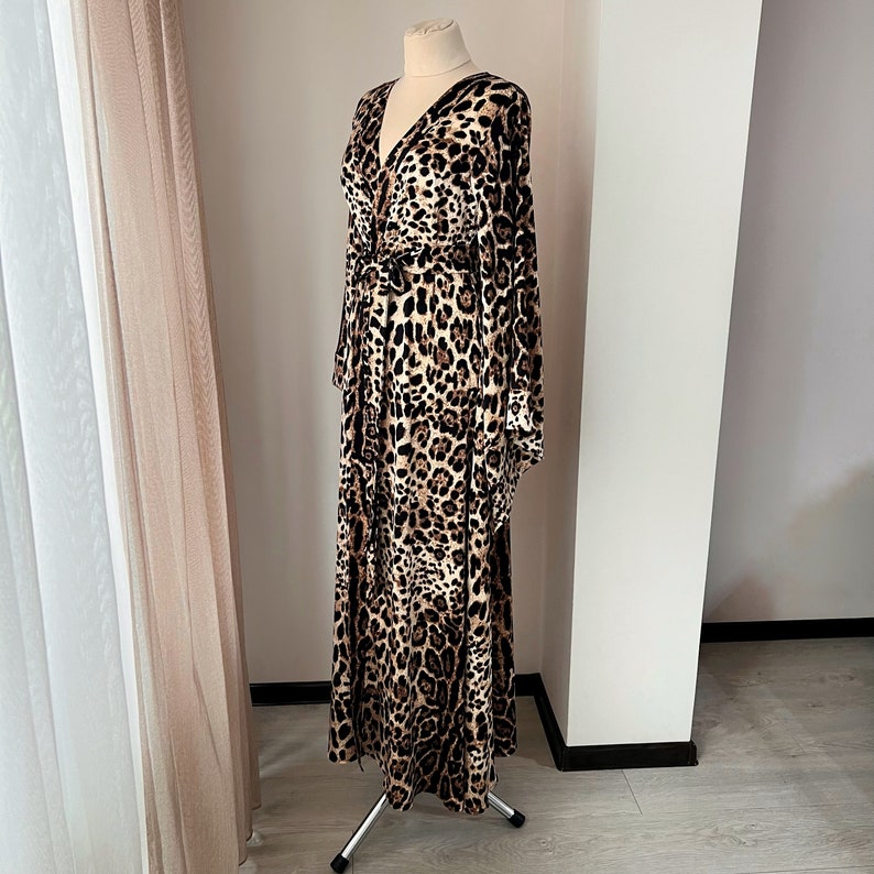 May include: A long, brown and black leopard print maxi dress with a V-neckline and long sleeves. The dress has a tie at the waist.