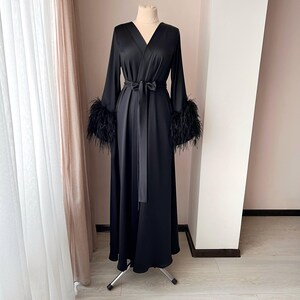 May include: A long black satin robe with a tie belt and feather trim on the cuffs.