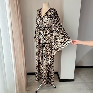 May include: A long, brown and black leopard print robe with a wrap style neckline and long, wide sleeves. The robe is made of a soft, flowing fabric.