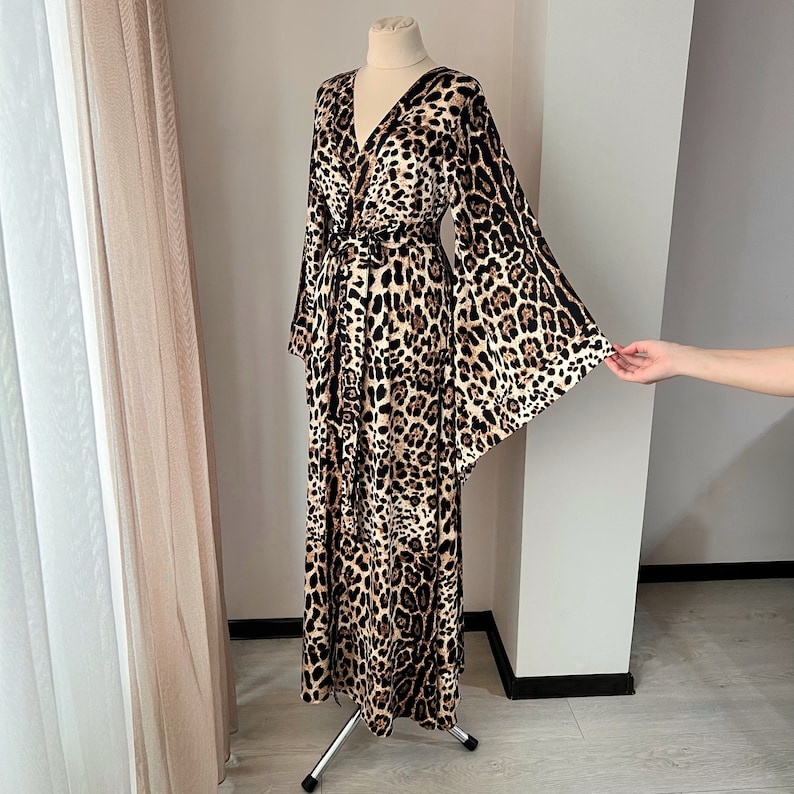 May include: A long, brown and black leopard print robe with a wrap style neckline and long, wide sleeves. The robe is made of a soft, flowing fabric.