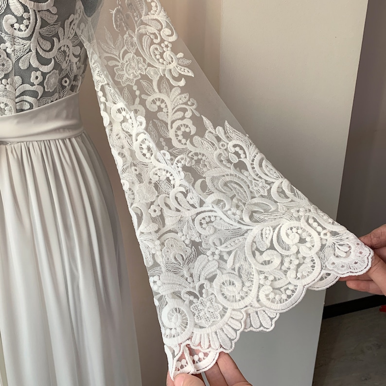 May include: White maxi dress with long sleeves featuring a delicate floral lace pattern. The sleeves are sheer and have a bell shape.