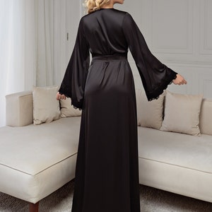 Peut inclure: Une longue robe de satin noire avec des bordures en dentelle sur les manches. La robe a une ceinture &agrave; nouer et un col en V.
