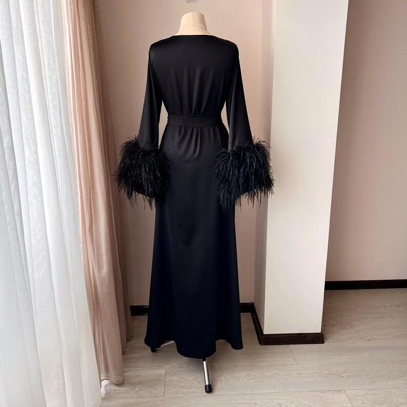 May include: A black satin robe with long sleeves and a sash. The sleeves have black feather trim.