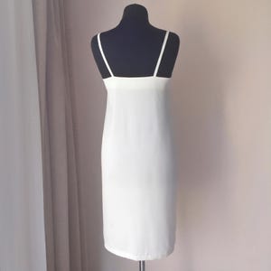 May include: A white slip dress with thin spaghetti straps and a straight neckline. The dress is displayed on a black mannequin against a neutral background. The dress appears to be made of a lightweight, flowing fabric.