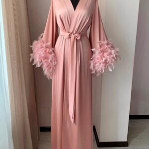 May include: A long, pink satin robe with feather trim on the sleeves. The robe has a sash tie at the waist.