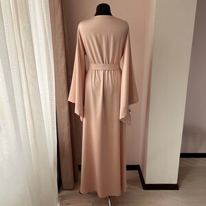 May include: A long, light pink robe with wide sleeves and a sash tie at the waist.