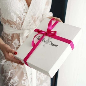 May include: A white gift box with a pink ribbon and the text "Bella Donna" printed on the top.