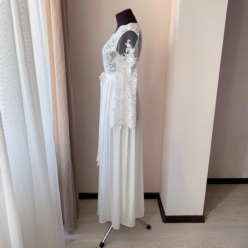 May include: A white lace robe with long sleeves and a flowing skirt. The robe is tied at the waist with a white sash.